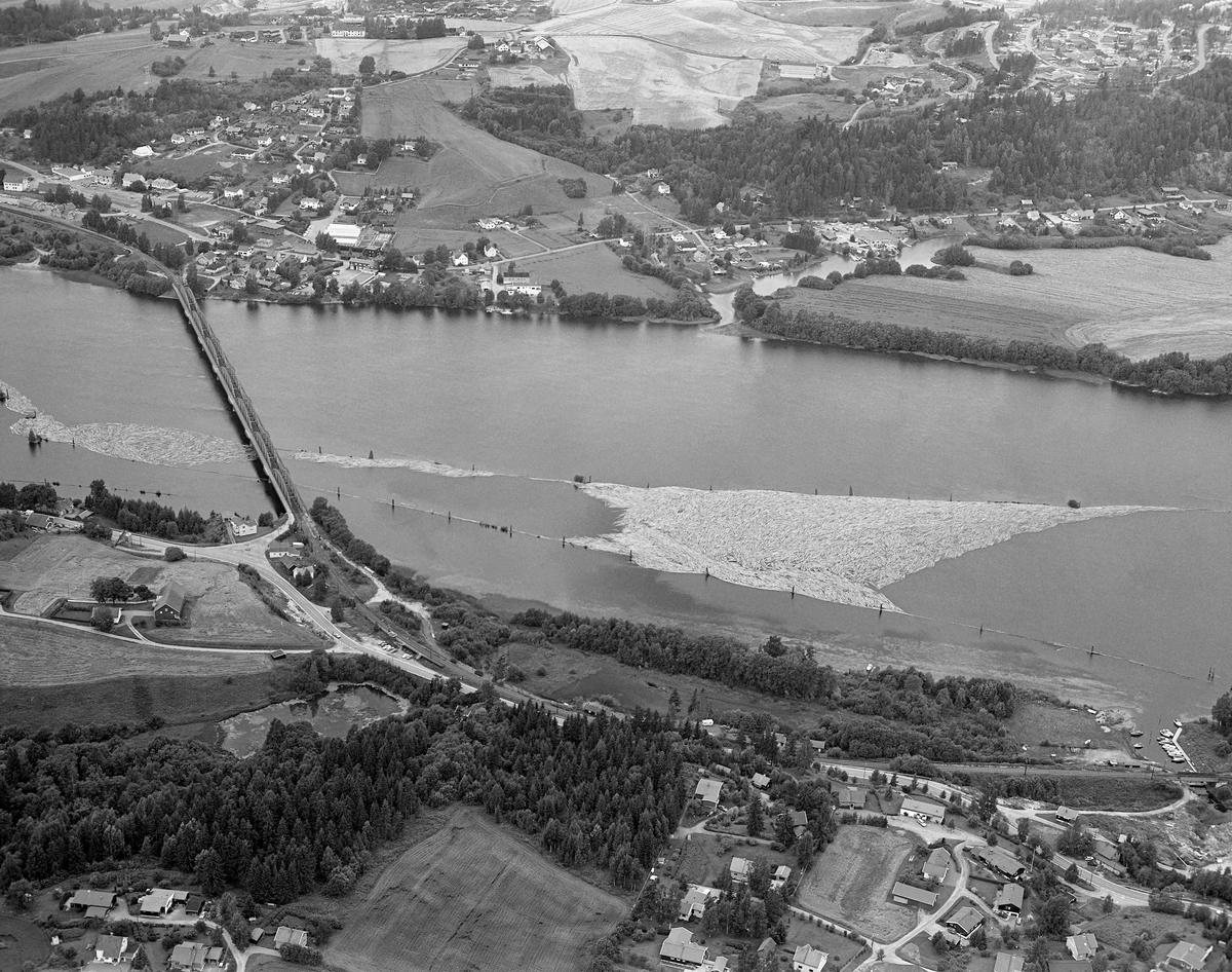 Flyfotografi, tatt over den øvre delen av lenseanlegget på Fetsund i Fet kommune i 1985, som var det siste året med tømmerføting i Glomma.  Vi ser ned mot det stilleflytende vannspeilet, der det stakk opp «gæljer» (pålekonstruksjoner) som var rammet ned i elvebotnen som støttepunkter for den traktformete lensa.  Da dette fotografiet ble tatt var det bare lenseinnretningene langs den vestre elvebredden som var i bruk (den lå til venstre for venstre bildekant).  Tømmeret ble sluppet porsjonsvis ned mot Fetsund fra attholdslensa ved Bingen, cirka åtte kilometer lengre nord.  1985 var det siste året det ble fløtet tømmer i Glomma, og dette året var det bare hovedvassdraget fra Rena i Åmot og sørover som hadde fløting.  Fløtingskvantumet hadde et volum på 126 014 kubikkmeter, som var et svært beskjedent tall sammenliknet med hva som var vanlig i dette vassdraget en generasjon eller to tidligere.  Siden 1978 hadde det bare vært Borregaard fabrikker i Sarpsborg som hadde kjøpt fløtingsvirke i Glommavassdraget, og følgelig var det heller ikke lenger nødvendig med sortering av virket etter påslåtte merker på stokkene.  Til venstre i bildeflata ser vi jernbanebrua, der Kongsvingerbanen krysser Glomma.