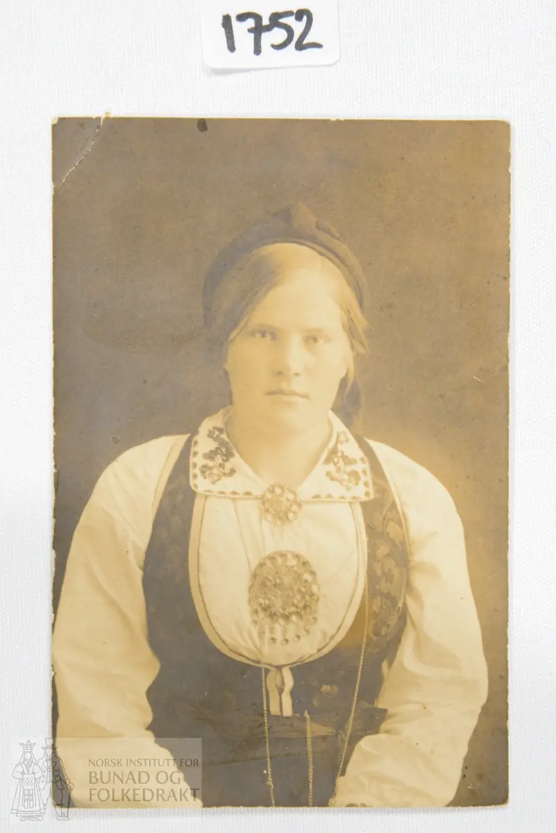 Portrett av kvinne. Hun er kledd i livstakk fra Vest-Telemark med rosesauma liv og sølvband. Klokkelenke rundt halsen.