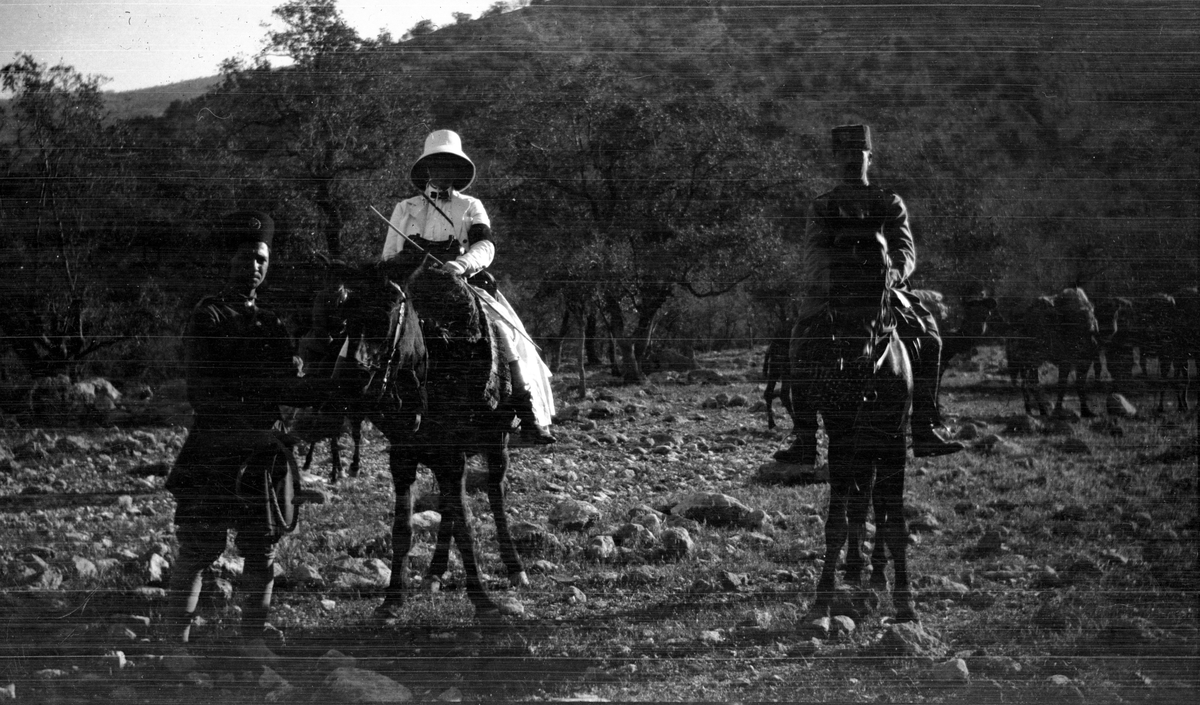 Ett par till häst (t v i ljus klänning Ida Uggla). En stående persisk gendarm håller i Fru Ugglas häst.