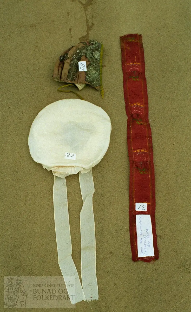 "Off-white" silke.  Rund fasong pyntet med bånd i samme type og "rosett" og bånd til å knyte.  Fôret med tyll.  Innv. diameter: 17 cm.