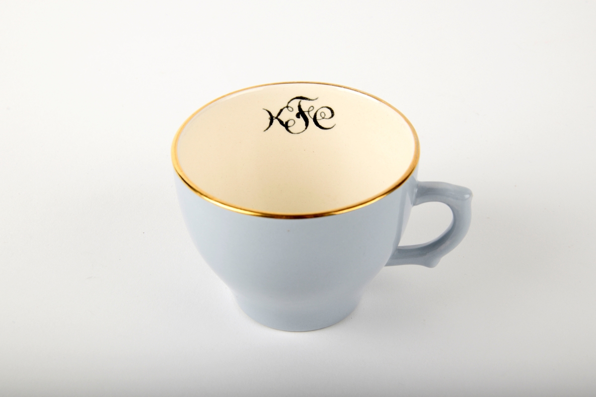 Kaffekopp med fat.

Koppen har monogram på innsiden. Både koppen og fatet har gullfarget kant.