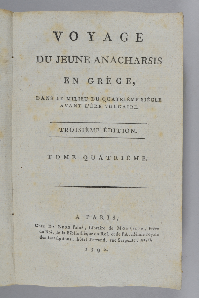 Bok, pappband, "Voyage du jeune Anacharsis en Grèce", del 4, tryckt 1790 i Paris. Pärmar av gråblått papper, på insidan klistrade sidor ur annan bok. Blekt rygg med bokens titel samt etikett med samlingsnummer. Skuret snitt.