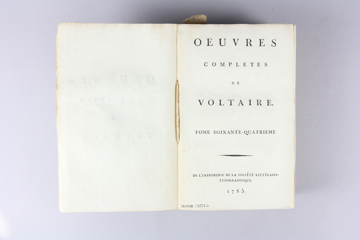 Bok, häftad, "Oeuvres completes de Voltaire, Lettres du Prince royal de Prusse...", del 64, tryckt 1785.
Pärmen av gråblått papper, på pärmens insidor klistrade sior ur annan bok. Med skurna snitt. På ryggen pappersetikett med tryckt text samt volymens namn och nummer. Ryggen blekt.