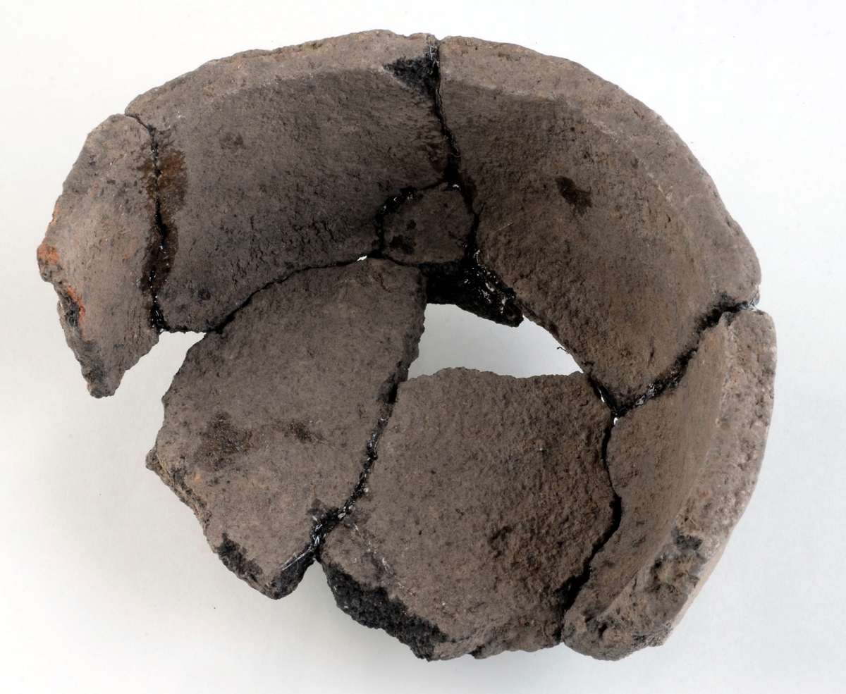 Kärl av keramik. Kärlet har en huvudsakligen plan, men något oregelbunden och klumpigt utförd mynning. Ungefär 50 % av kärlet är bevarat. Kol påträffat tillsammans med kärlet 14C-daterades till yngre romersk järnålder/folkvandringstid, eller 340–510 e Kr (Ua-51189).