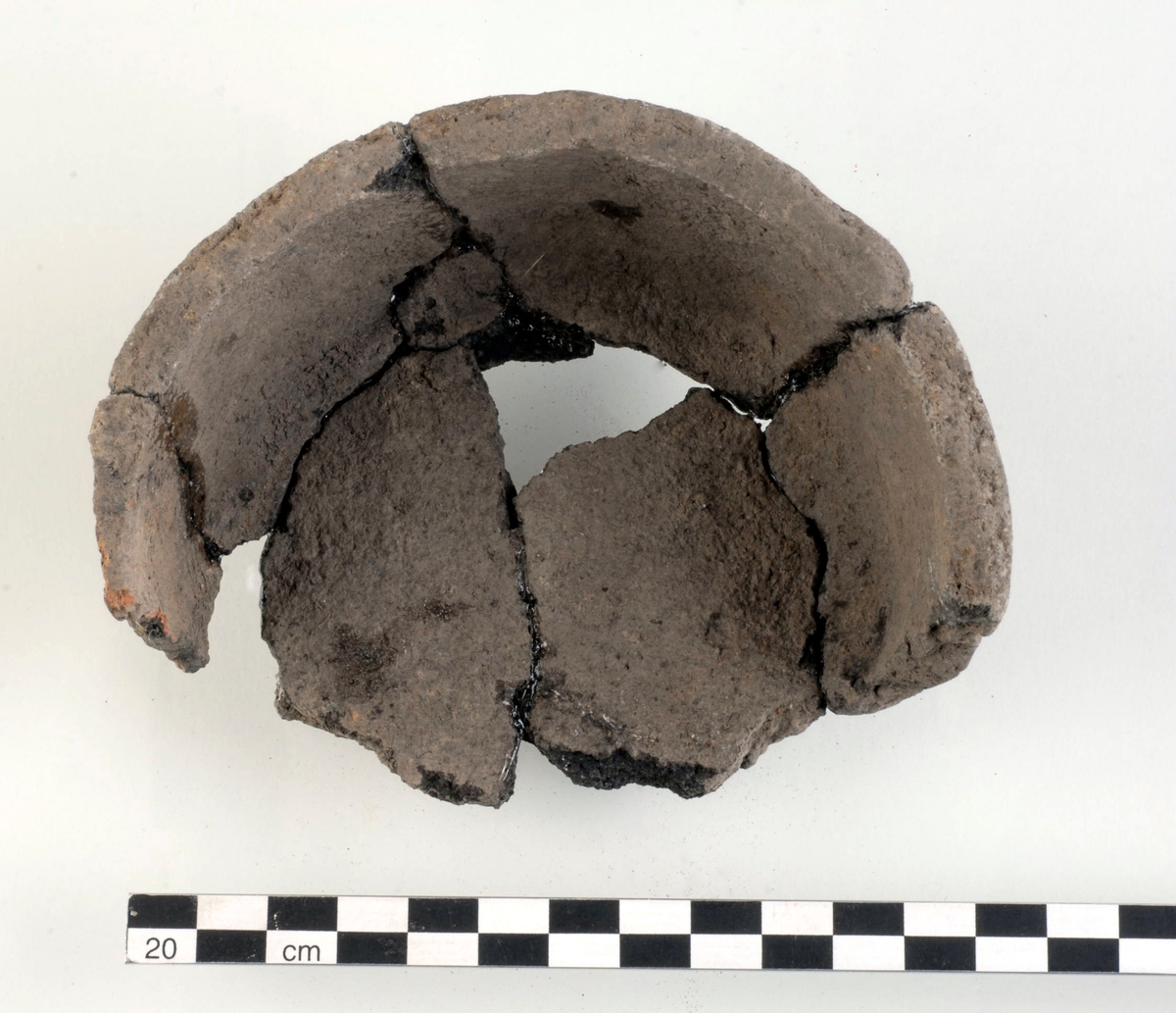 Kärl av keramik. Kärlet har en huvudsakligen plan, men något oregelbunden och klumpigt utförd mynning. Ungefär 50 % av kärlet är bevarat. Kol påträffat tillsammans med kärlet 14C-daterades till yngre romersk järnålder/folkvandringstid, eller 340–510 e Kr (Ua-51189).