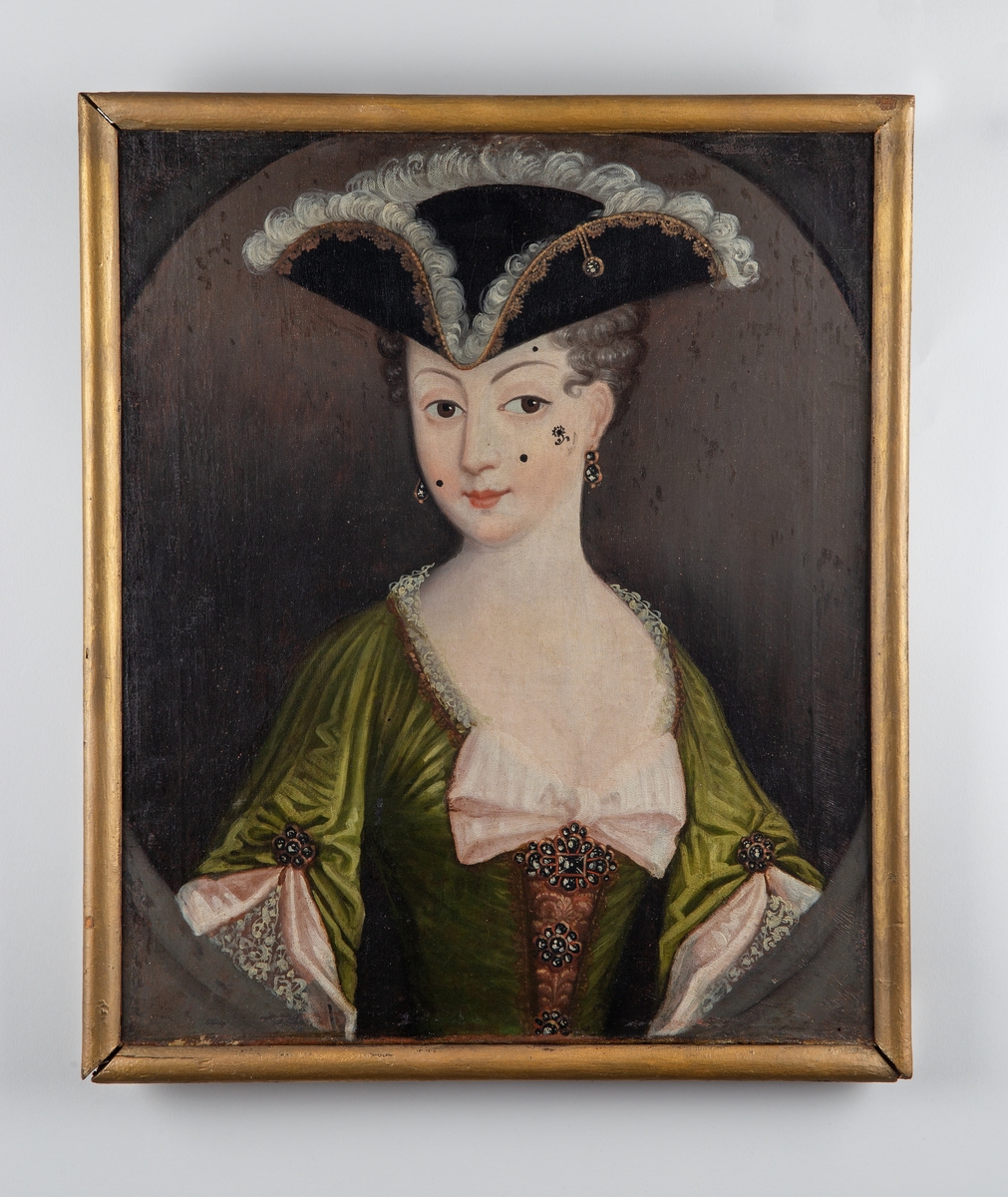 Kvinneportrett, brystbilde, grønn kjole, sort 3-snutet hatt, blekrosa sløyfe på brystet.