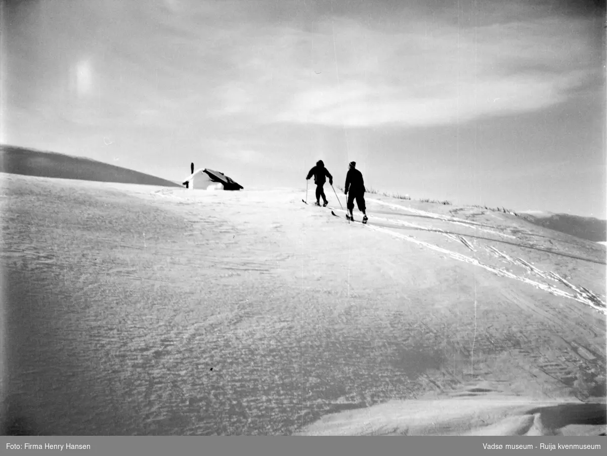 Vinikka. Vinter og sne. 2 skiløpere på vei mot en hytte.