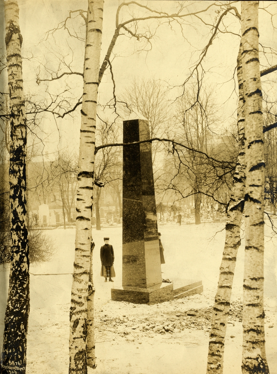 Henrik Ibsens gravstøtte på Vår Frelses Gravlund. Gravstøtten (laget av Labrador stein) er levert av Erik A. Gude. To ukjente mennesker står ved graven.