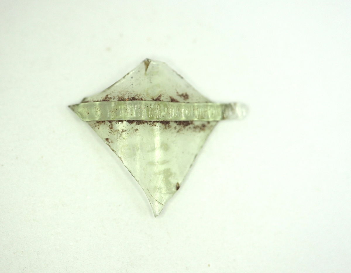 Fragment av ett gröntonat, optikblåst passglas med pålagd strierad glastråd. Ursprungligen mångkantigt.