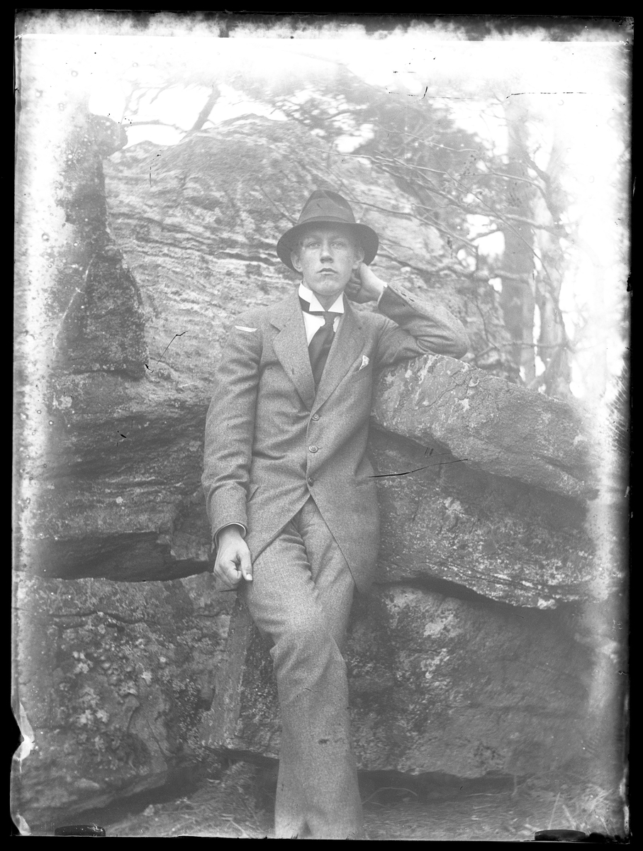 Porträtt av Gusten Hansson iklädd kostym och lutande mot en sten.