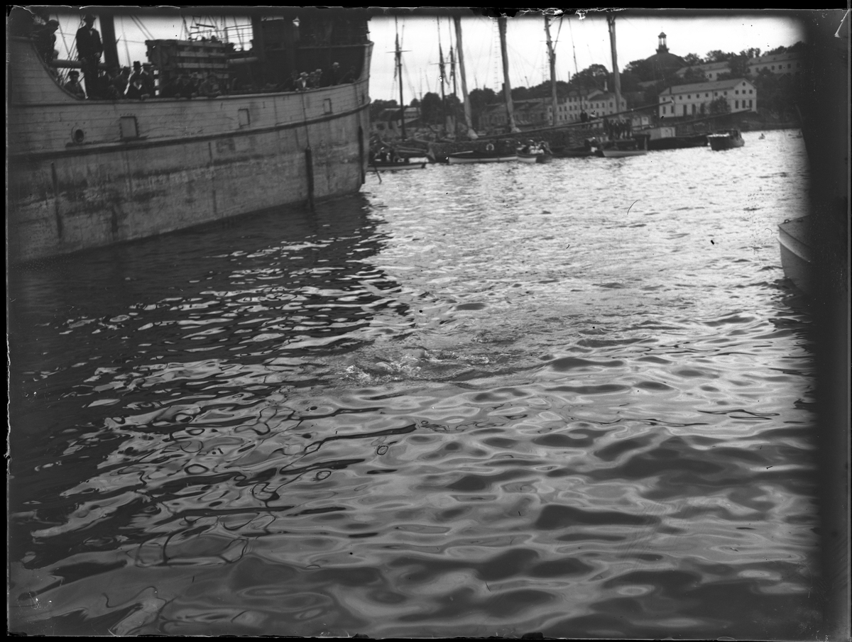 Bild tagen från Skeppsbrokajen över vattnet mot Skeppsholmen och Skeppsholmskyrkan. Ett antal skepp syns. Bilden togs under fotografen Harald Olssons excercistid.