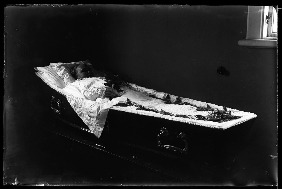 Tilda Pettersson fotograferad avliden med en blombukett i handen liggande i sin kista. Kistan har dekorerats med liljekonvalj.