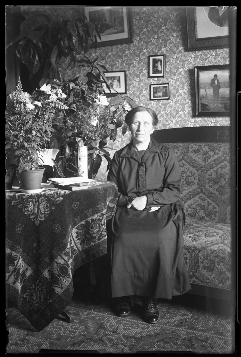Augusta Ax fotograferad sittandes i en soffa i ett finrum i samband med sin 60årsdag. Bredvid henne på ett bord står blommor och kort.