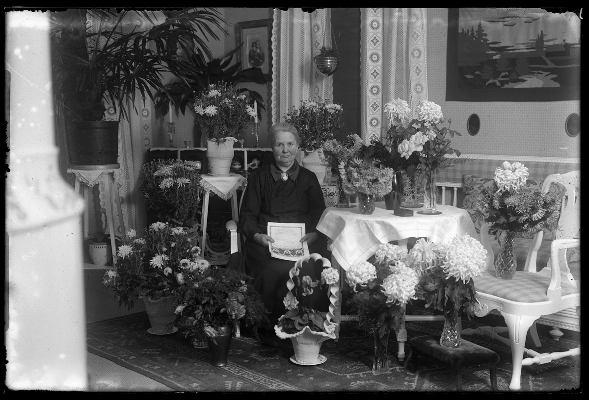 Fru Axelsson fotograferad med gratulationstelegram i handen och omgiven av blommor i samband med sin 50årsdag.