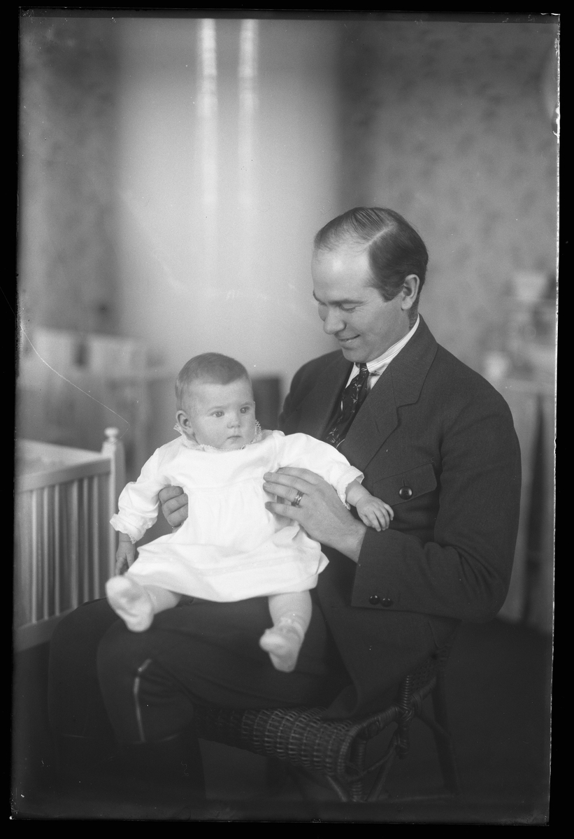 En leende man sitter i en barnkammare med sin dotter i knät. I fotografens anteckningar står det "Ing[enjör] Berg med dotter". Tolkat som Gunnar Teodor Berg med dottern Elsa Margareta.