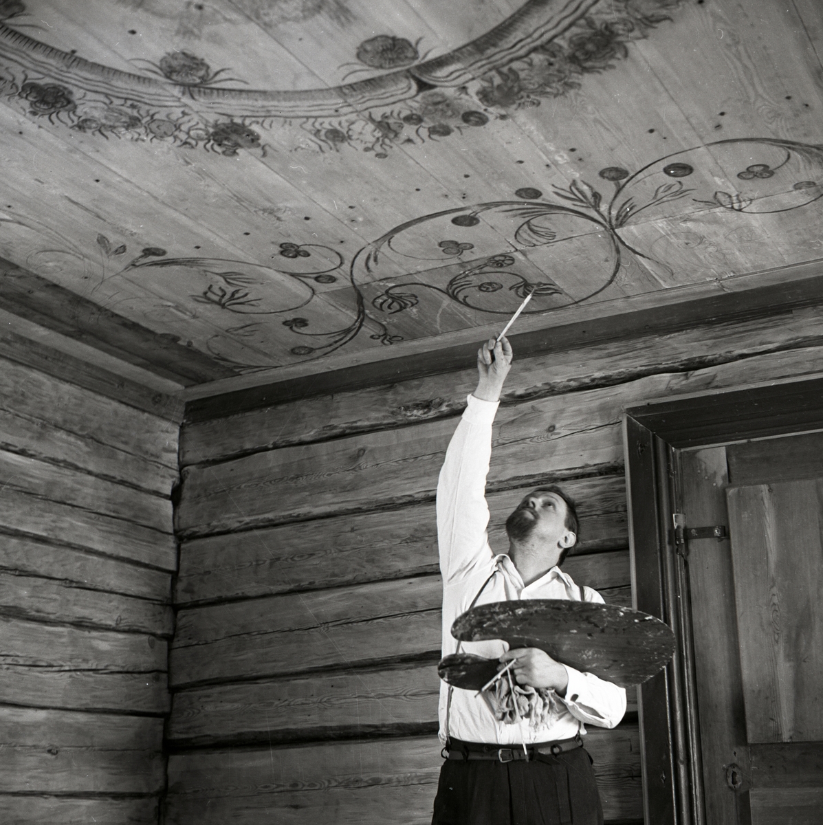 En man målar en takdekorationen vid byggnaden av gården Sunnanåker, 1968-1969.