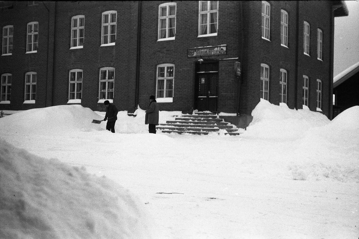 To bilder fra Lena sentrum februar 1954. Bildene viser to uidentifiserte menn foran Narums-butikken, den ene rydder snø.