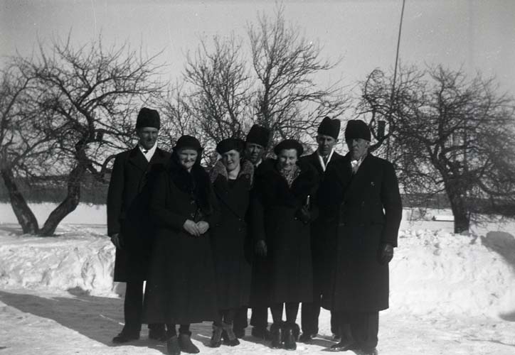 En grupp mörkt klädda personer poserar framför några äppelträd under vinterhalvåret, 1940.