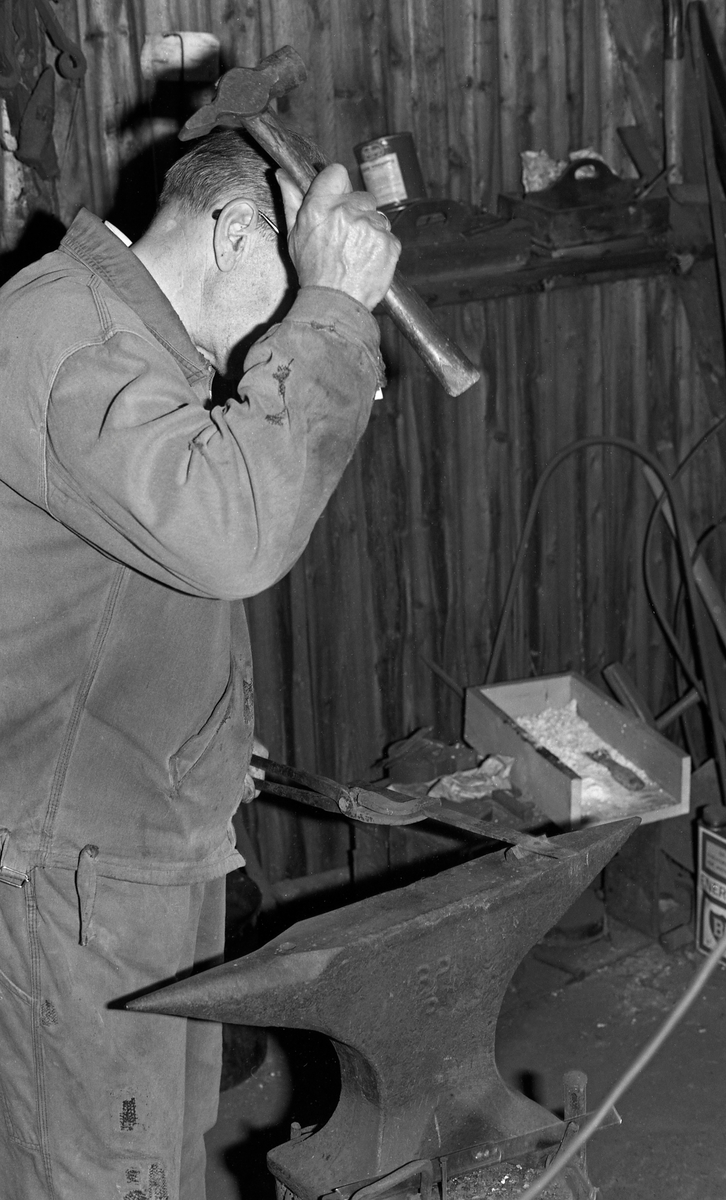 Knivmakeren Even Johannes Blindingsvolden (1908-1985) fra Ringsaker, fotografert ved ambolten i smia, der han kappet et knivblademne som han holdt med ei tang på en meisel ved hjelp av kraftige hammerslag.  Den på dette tidspunktet 65 år gamle håndverkeren var kledd i dongeriklær mens han arbeidet.  Blindingsvolden eide og bodde på småbruket Rudsland på Rudshøgda.  Her hadde han et et 43 kvadratmeter stort hus ved Prestvegen som inneholdt smie- og verkstedrom.

Mer informasjon om knivsmeden Even Blindingsvolden finnes under fanene «Bildehistorikk» og «Opplysninger».