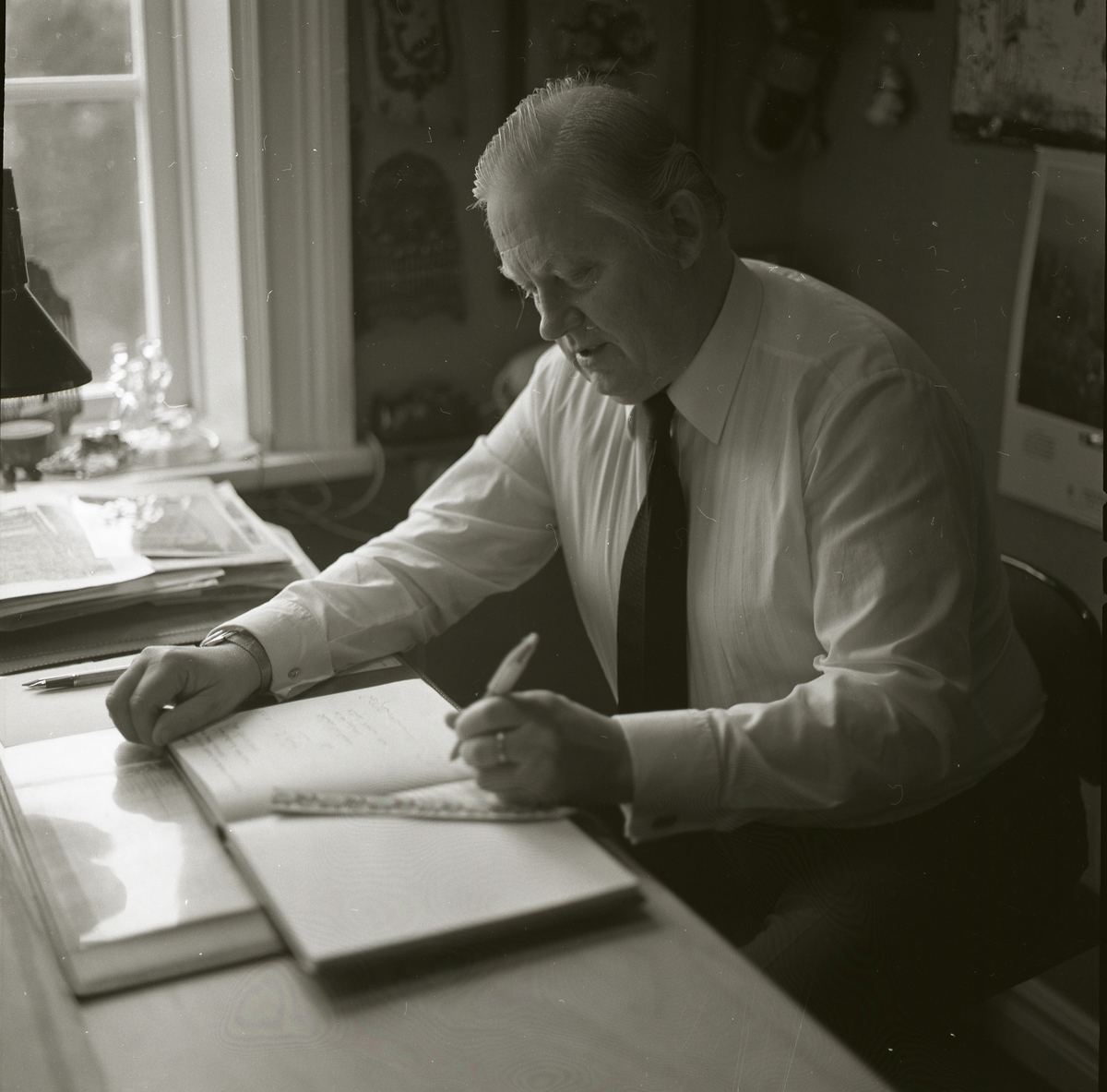 Bo Setterlind, författare, poet och psalmdiktare,  sitter vid ett skrivbord med en öppen bok framför sig och en penna i handen, 20 oktober 1985.
