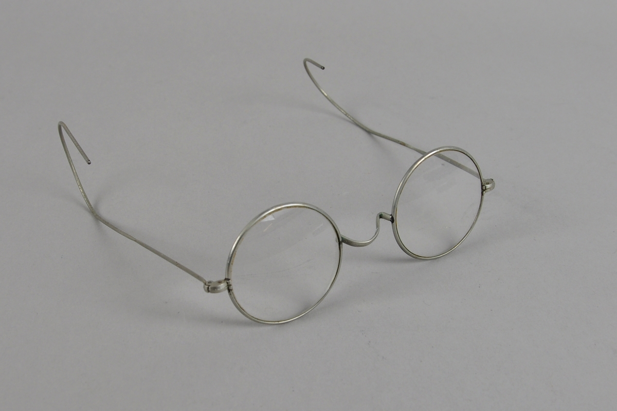 Runde brilleglass med metallinnfatning. Brillestengene er buede ytterst.