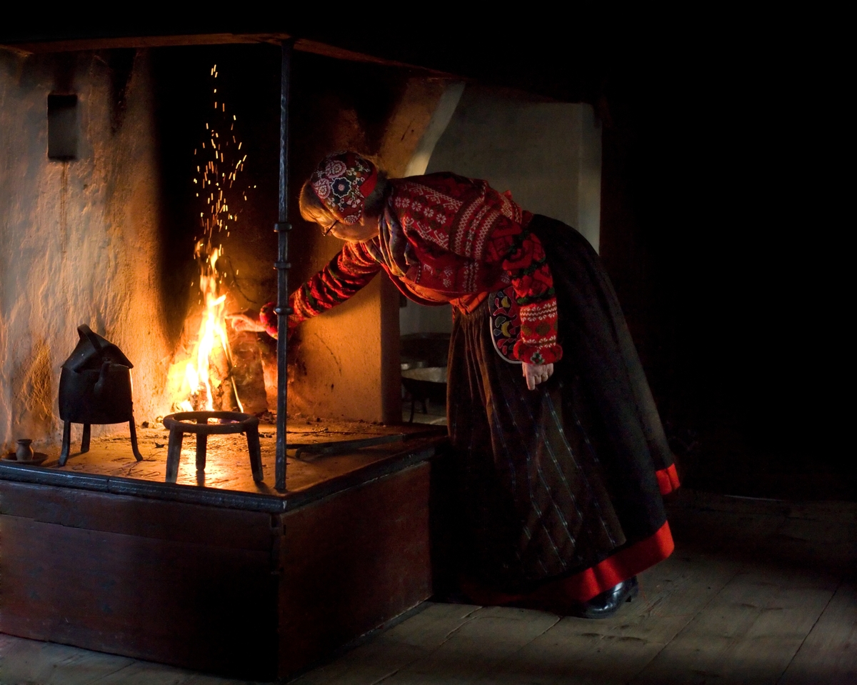 Interiör från en Skansenmiljö. Eldstad, pedgagog klädd i folkdräkt.