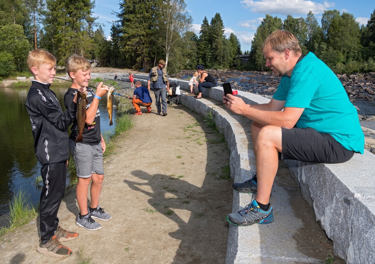 Pappa Stein Tore Andersen fotograferer sine to sønner Marius Bakkedal- Andersen (t.v) og Eirik Bakkedal- Andersen med fin ørret som de har fisket i fiskedammen på Norsk skogmuseum under De nordiske jakt- og fiskedager 2018.