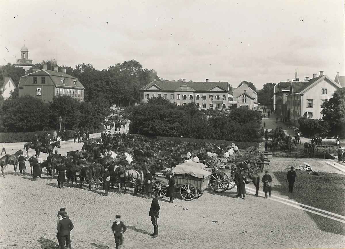 Kungliga Första Göta artilleriregemente rastar på Lilla Torget på marsch till Tåga hed, sommaren 1900. I bakgrunden syns Stora torget.