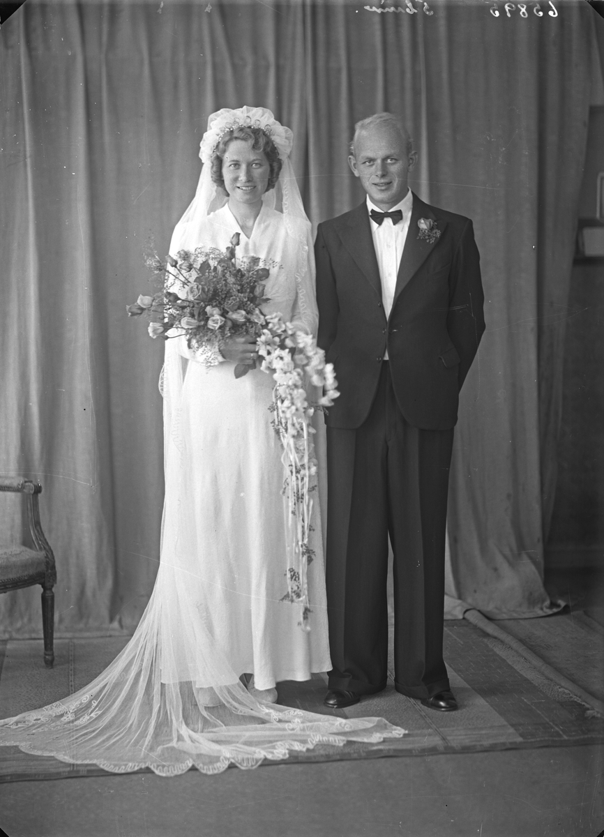 Portrett. Ung kvinne i hvit brudekjole med blomsterbukett og ung mann i mørk dress. Brudepar. Bestilt av Johannes T. Skåren. Utsira