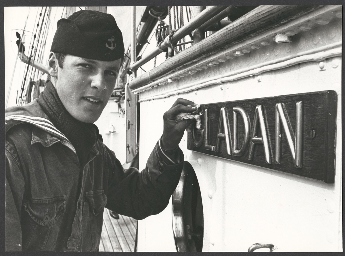 Bilden visar en kadett på Marinens skolfartyg Gladan som håller på att polera namnbrädet.