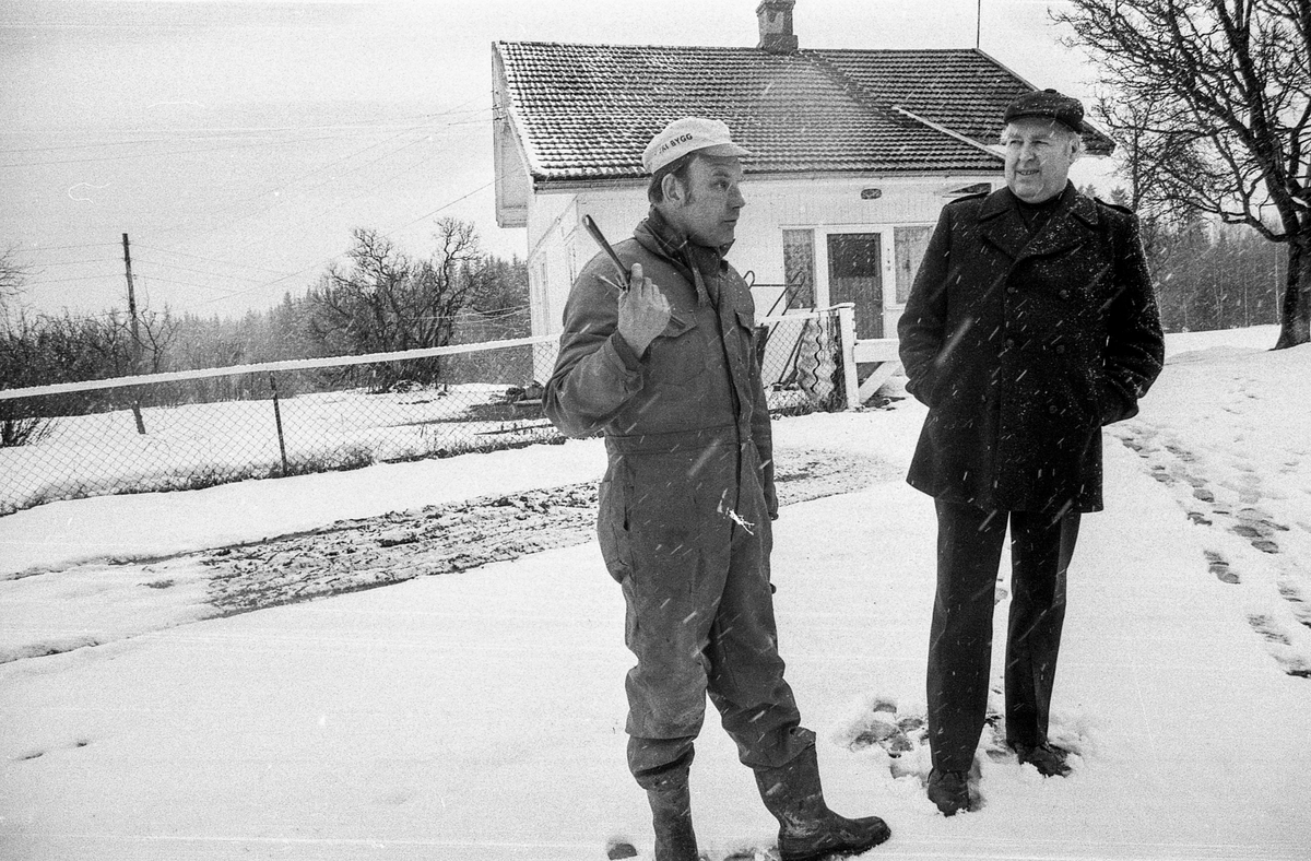 Nylenna i Ski, en utkantbygd. To menn snakker sammen en grå vinterdag, den ene i kjeledress.