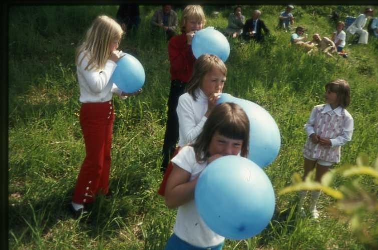 75-årsminnet av Andrées Nordpolsfärd firas Ballongdagen på Åsavallen i Gränna 1972. Flickor och pojkar som blåser upp blå ballonger. På slänterna sitter publiken. Diabild.