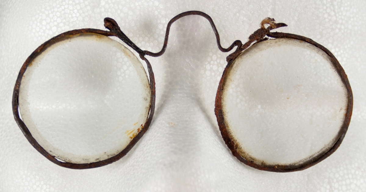 Lorgnett. Brille utan stenger. Med to runde glas, tynn metall innfatning og innretning av ståltråd til å feste brilla over naseryggen.