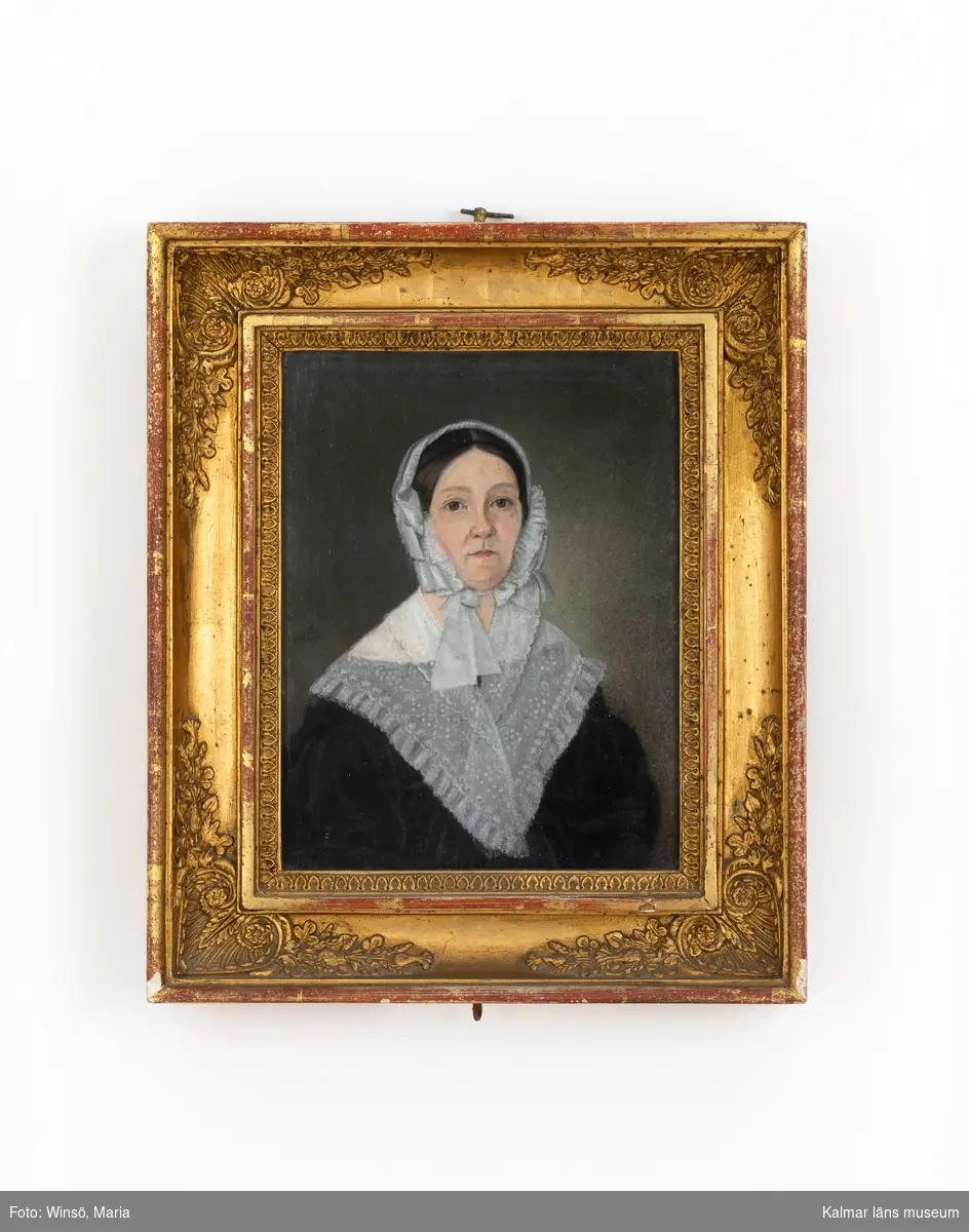Porträtt av en kvinna, prostinna, klädedräkt med tunn schal och huvudbonad med rosett.