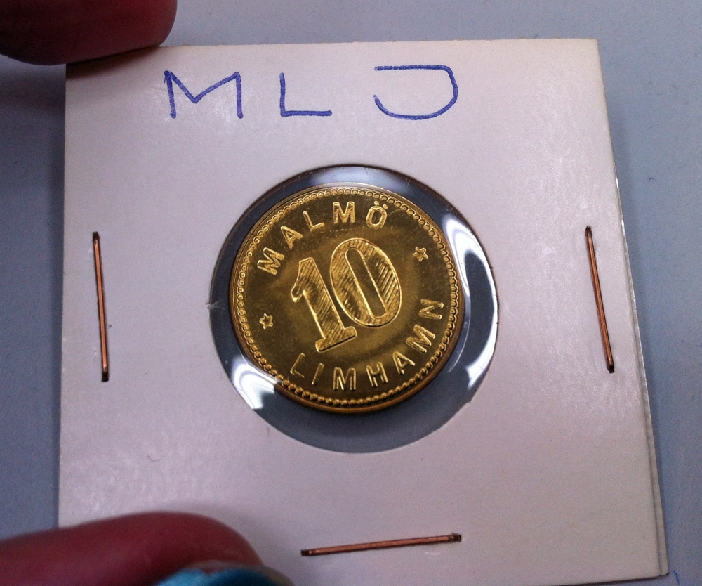 Minnesmynt från MLJ, troligen stansat och av mässing. Myntet är monterat i en kartongficka med runt plastfönster genom vilket man kan se myntets båda sidor.
På den ena sidan står följande:
"Malmö Limhamn 10"
och på den andra sidan:
1889 1989 tillsammans med ett vinghjul för Enskild Järnväg i mitten av myntet.