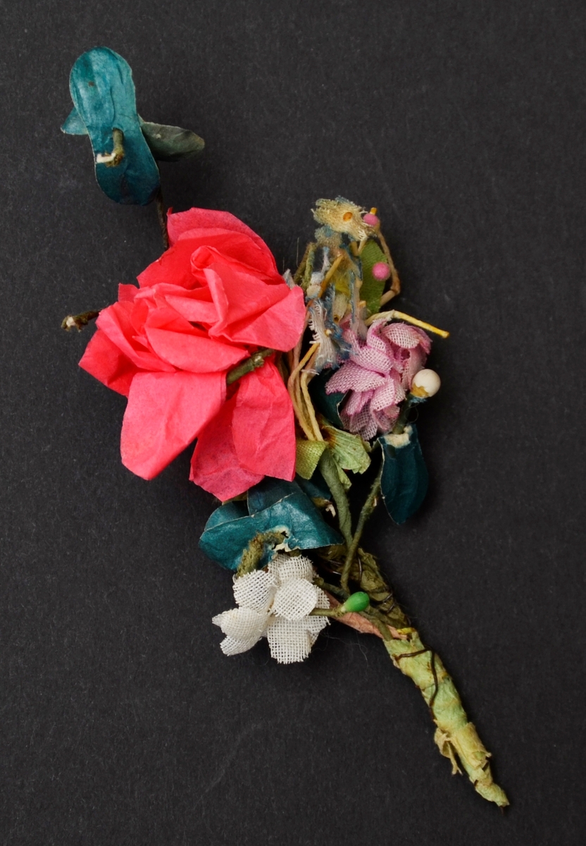 Knappholblome til brud. Blomer i rosa og kvitt, grøne bladar. Laga i tekstil og papir. Montert med tynn metall tråd.