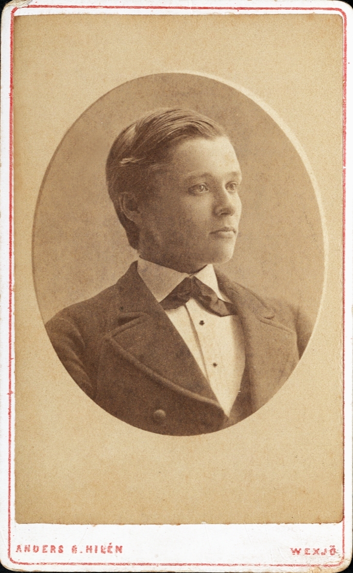 Porträtt (bröstbild, halvprofil) av en okänd man i kostym och stärkkrage med fluga. 

Bildtext: (baksidan) Fotografi af Anders Gust. Hilén, Wexjö.
