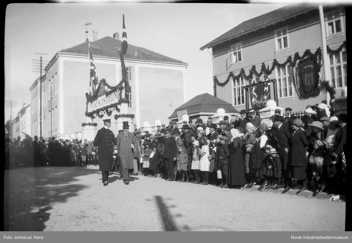 Åpning av Fylkesutstillingen 1922 med besøk av Kong Haakon VII. HM Kongen går igjennom gatene, folkemengde langs gaten.