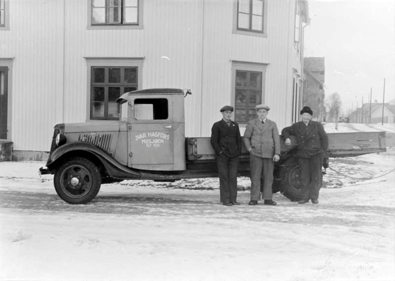 Lastebilen (Ford 1935-modell) til Ivar Hagfors oppstilt utenfor huset til Ivar Hagfors i krysset Chr. Qvales gate / Torolfs gate. Fra v. Arne Greger, Ivar Lund Hagfors og Nils Hagfors.