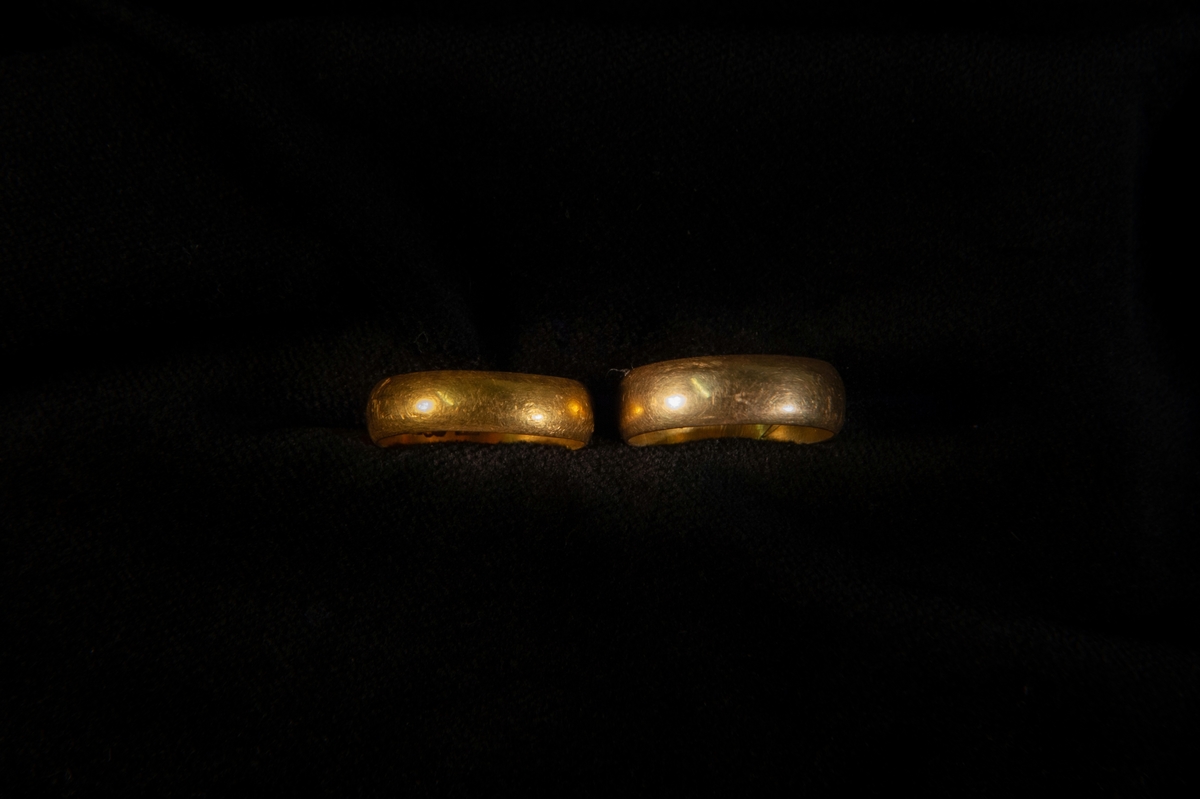 Två vigselringar av guld, bred, kupig. Förvaras tillsammans med ringen 22794:2 i en röd pappask.