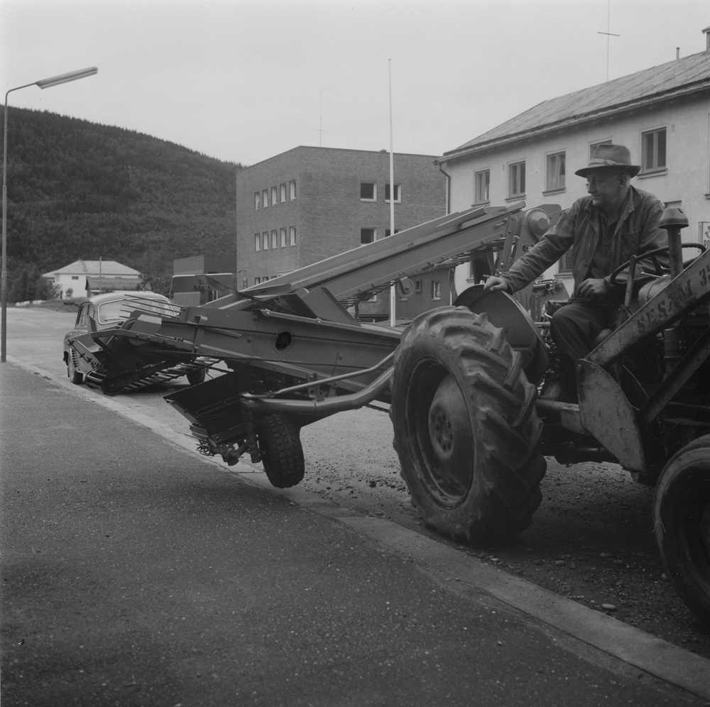 Mann med traktor med potetopptaker i Fearnleysgt. 
I bakgrunnen postkontoret og telegrafen.
Den første automatiske potetopptaker i Vefsn.