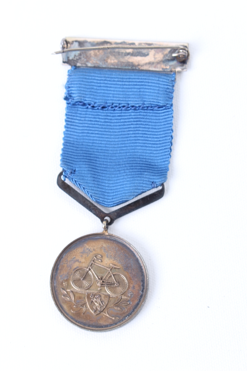 Sirkulær medalje med blått medaljebånd og agraff.