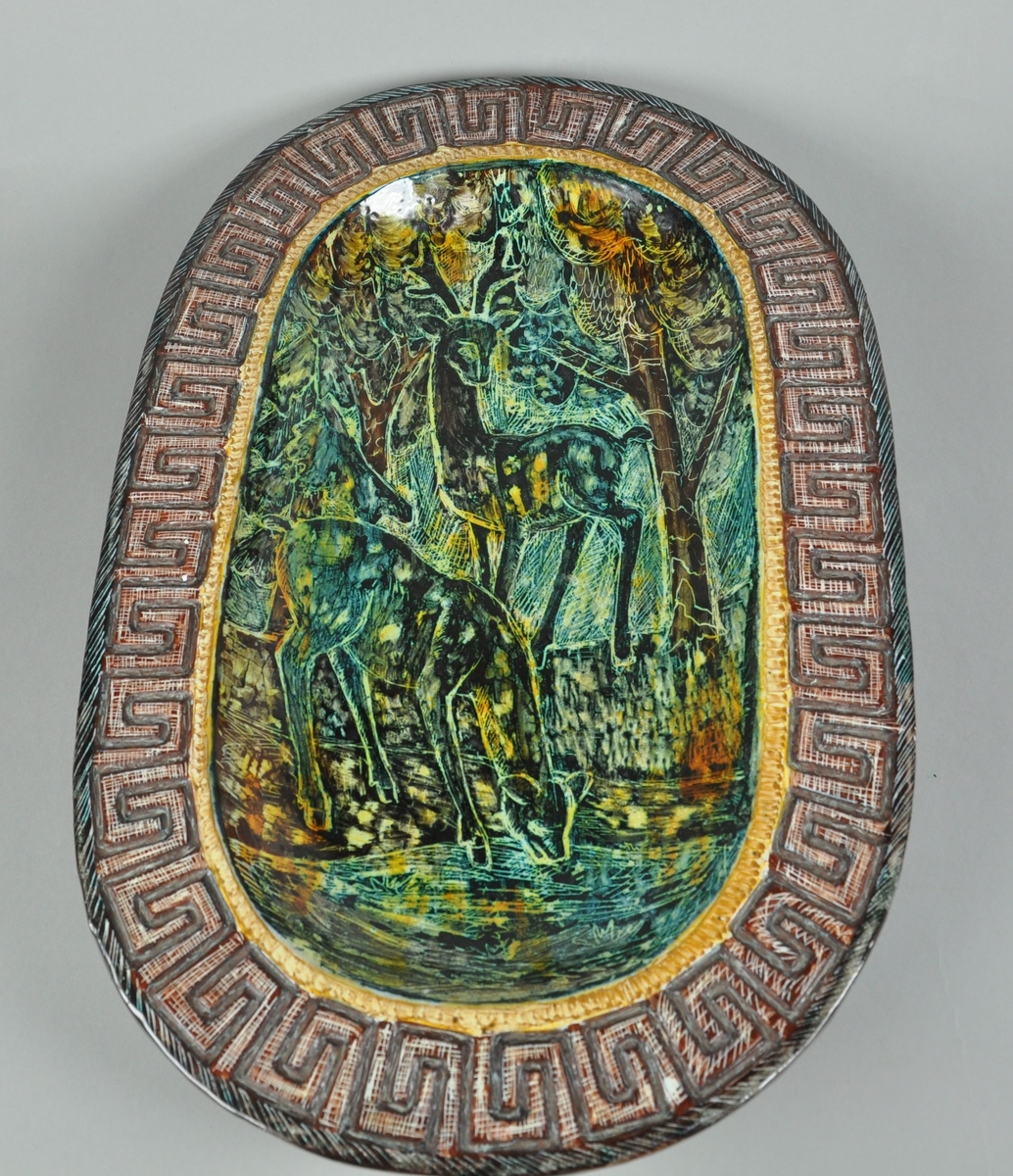 Ovalt fat av glassert keramikk. Fatet har utstående kant. Langs kanten går det en borde med gresk mønster. I fatet er det motiv av to rådyr ved et vann.