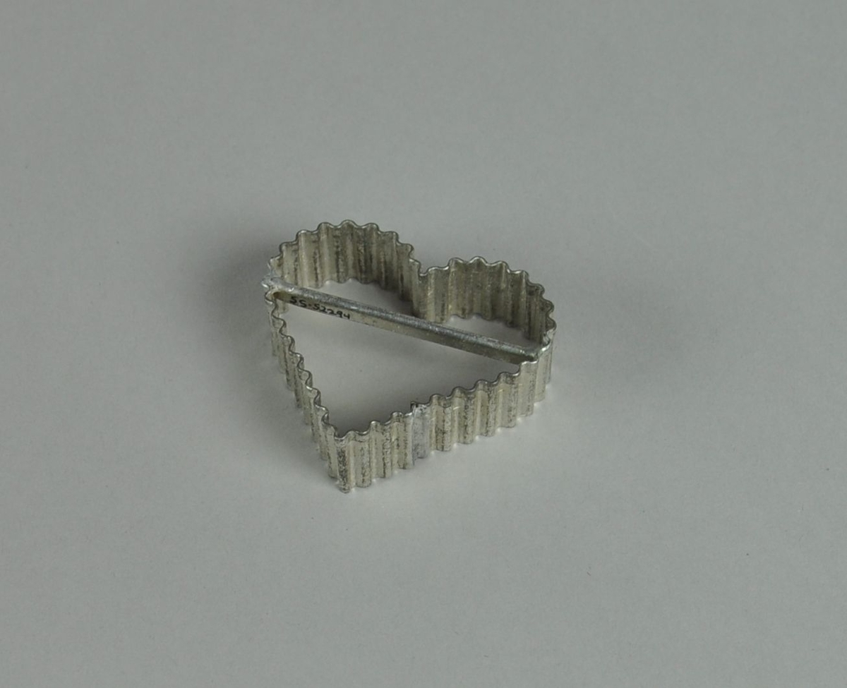 Kakeform av aluminium. Hjerteform med bølgete profil og hank på midten.