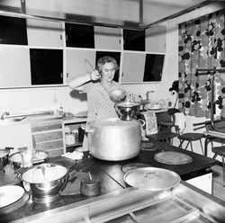 En kvinne øser mat til serveringsskål, på kjøkken på elevhei