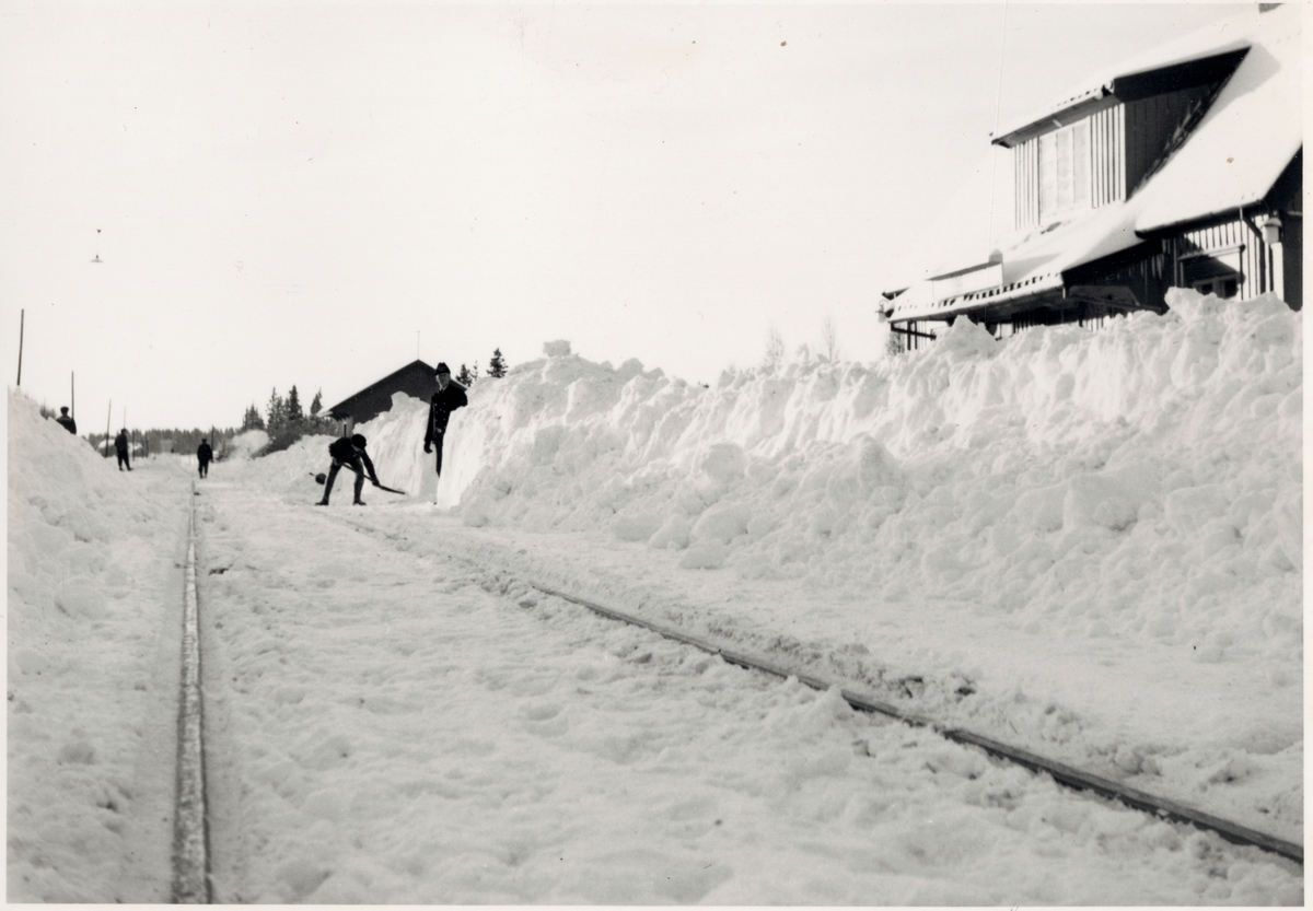 Vy på spår och stationshus med snövallar och pågående snöröjning ...