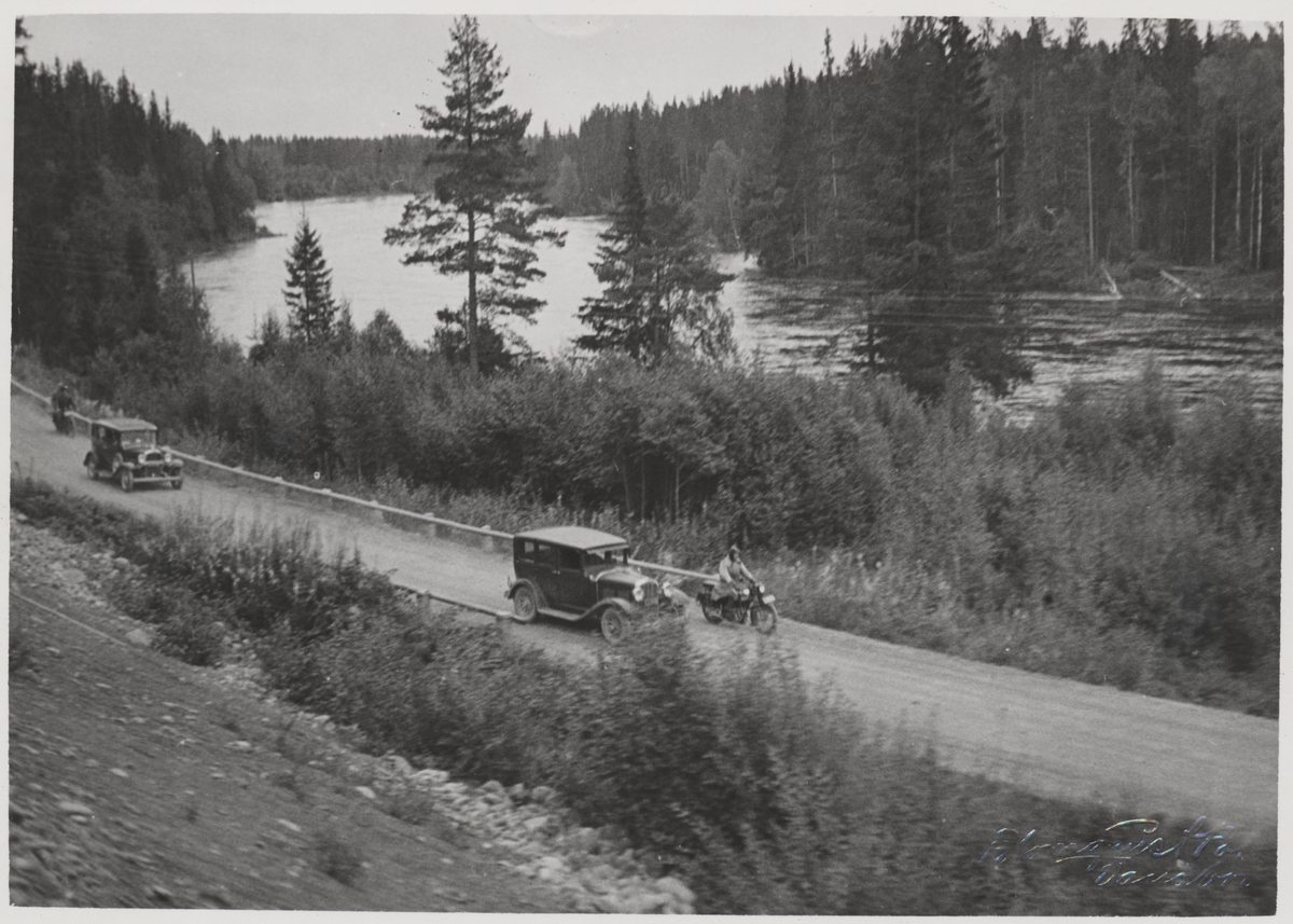 Två bilar och två motorcyklar på landsvägen mellan Vansbro och Malung vid Västerdalälven strax söder om Hovaforsen. Detta under invigningsdagen för Statsbanan Malung-Vansbro.