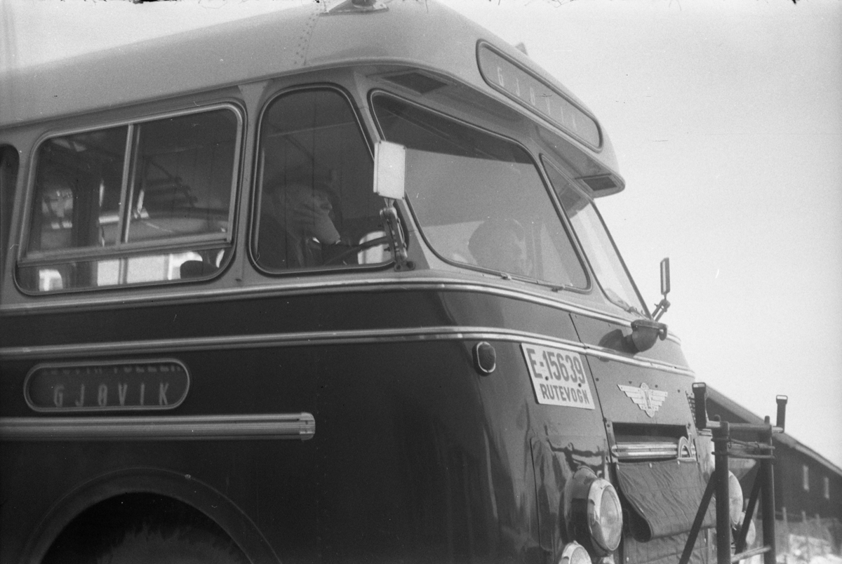 Fronten på en buss med kjennetegn E-15639 fotografert rett ut for "Raubua" på Lena mars 1955. To utydelige og uidentifiserte menn inne i bussen. Bussen er iflg. informanter en Volvo (logoen delvis skjult av radiatortrekket) B617 1954-modell, kjøpt ny av A/L Østre Toten Bilruter. Karosseriet ble bygd ved Larvik Karosserifabrikk, og fabrikkens logo ses midt over radiatoren.