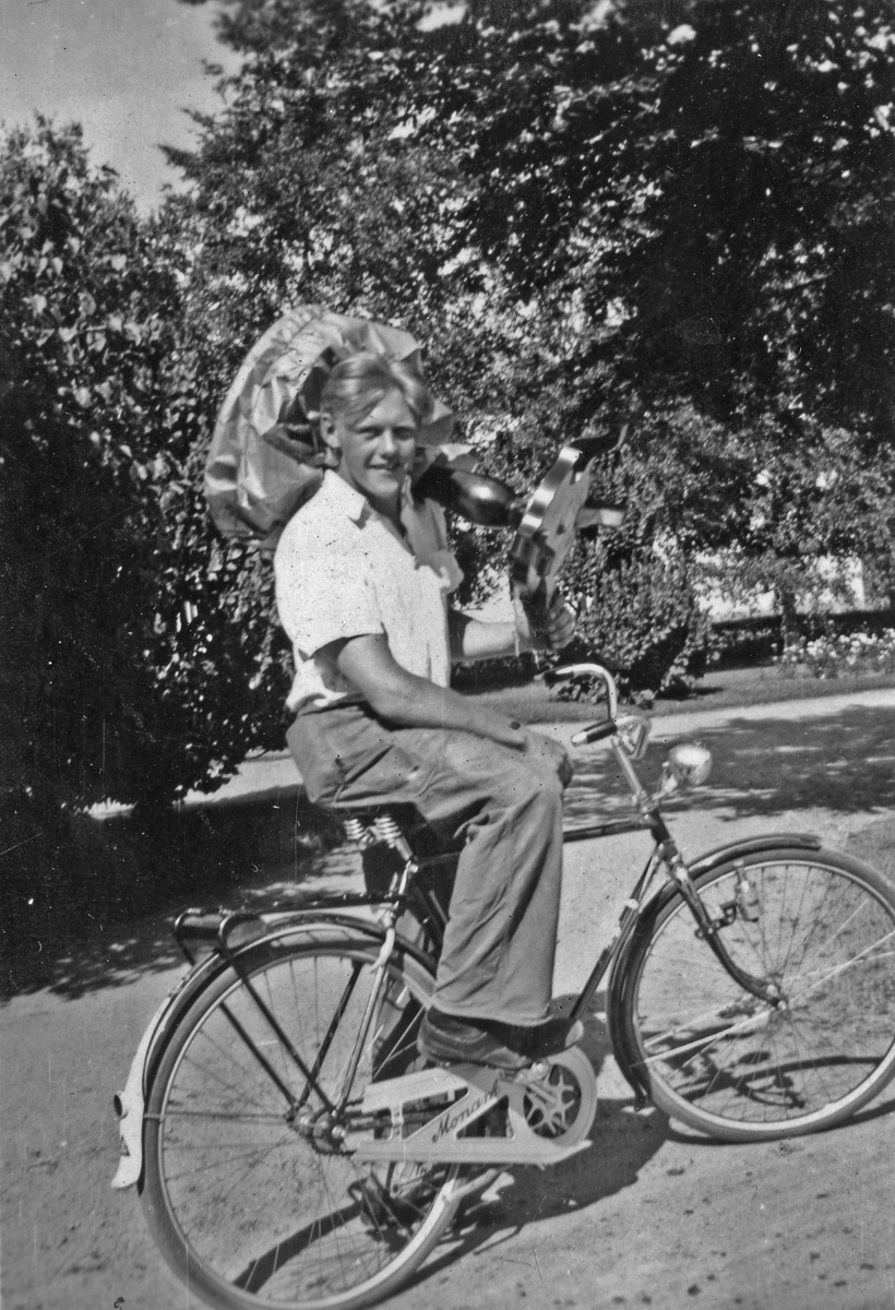 En ung man sitter på en cykel av märket monark och håller ett mindre bord i handen. På kortet står anteckningen "Berners gågosse" och syftar till springpojken på Berners Heminrednings butik.