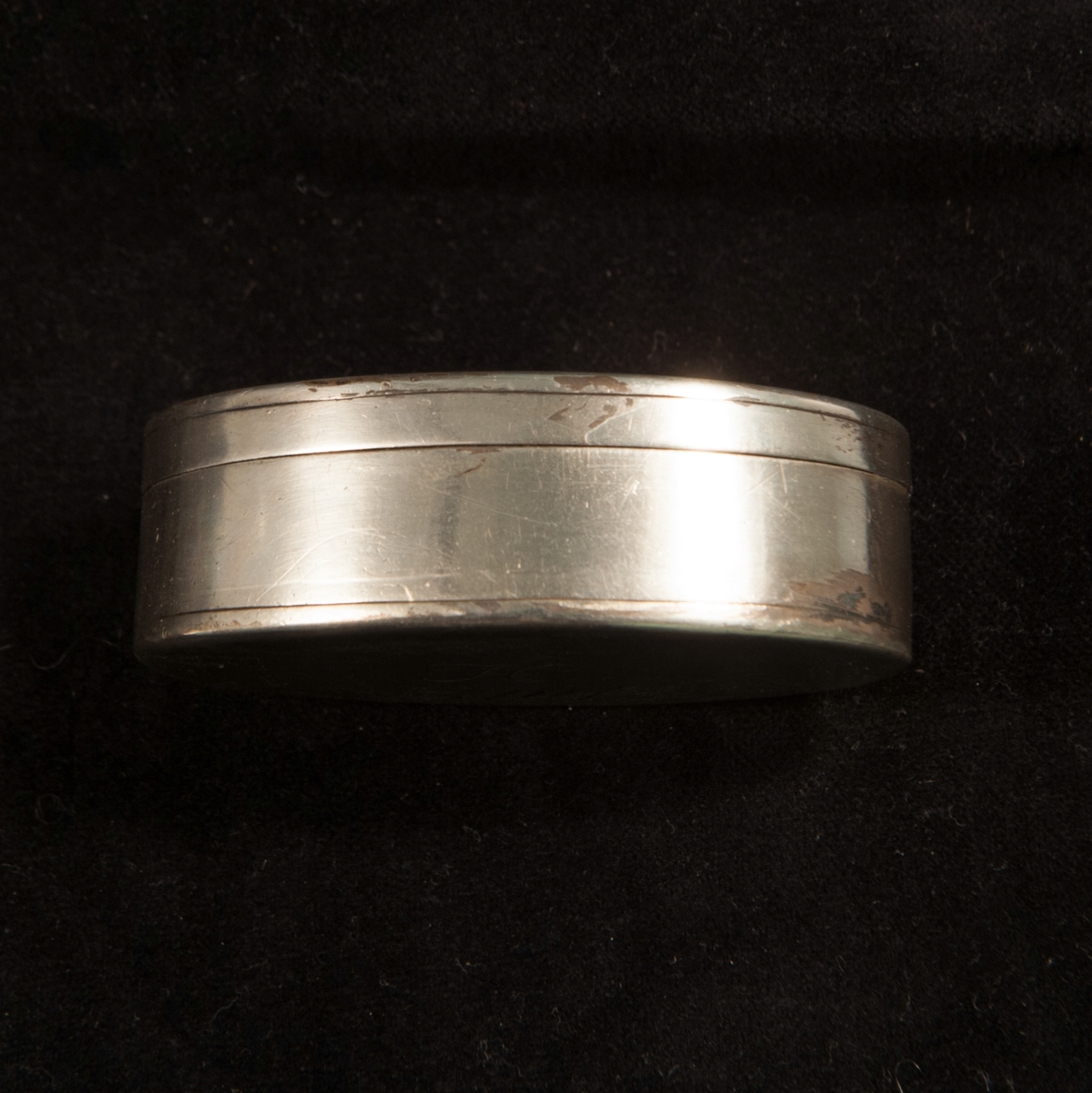 En oval dosa av silver. Slät modell med randdekor. I botten graverade ägarinitialer i spegel monogram: "JH ". Invändigt förgylld. Stämplad invändigt i botten.